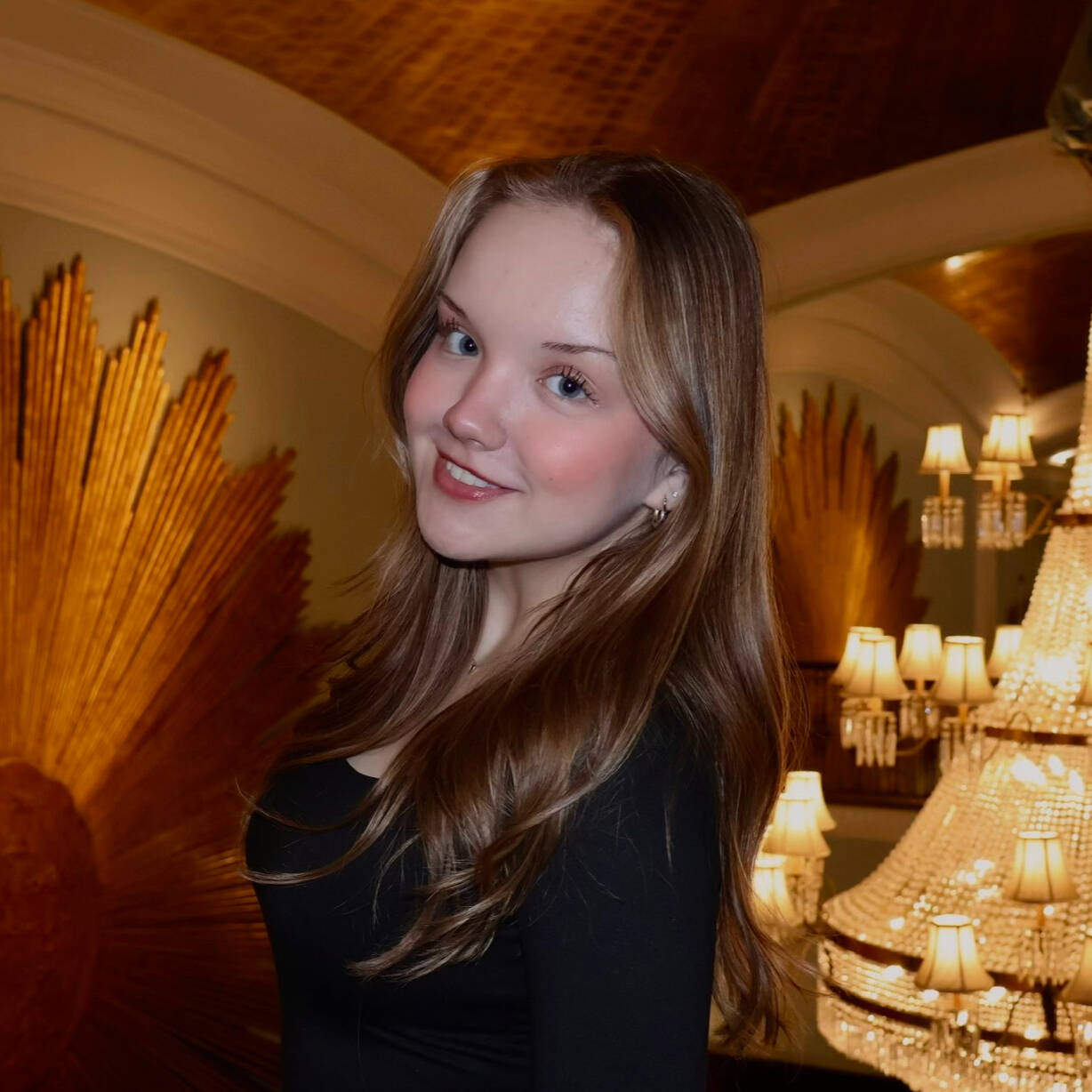 Smiling young blonde woman in the foreground with chandeliers in background